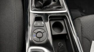 Car center console with gear shift boot, electronic parking brake button, circular drive-mode dial, cup holder, and keys in a tray.