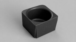 Dark square block with a circular hollow on the top surface, resting on a light gray background.