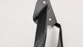 Close-up of a black brushed-metal strap with two circular holes, curved against a light background.