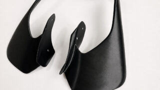 Abstract black sculptural form made of curved leather-like panels on a white background.